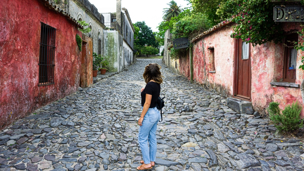 A woman standing in the middle of a historical cobblestone street, with colorful houses in Colonia del Sacramento, Uruguay.