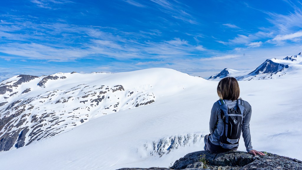 A young woman sitting at the top of a snow covered glacier in Seward, Alaska.