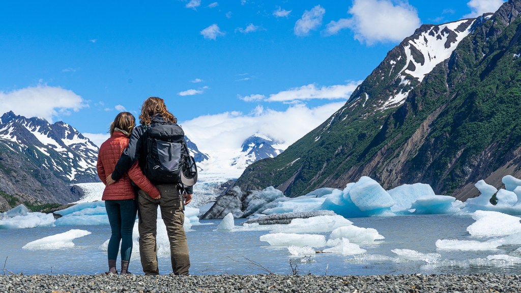 A young man and woman standing in front of a glacier lake in Alaska.