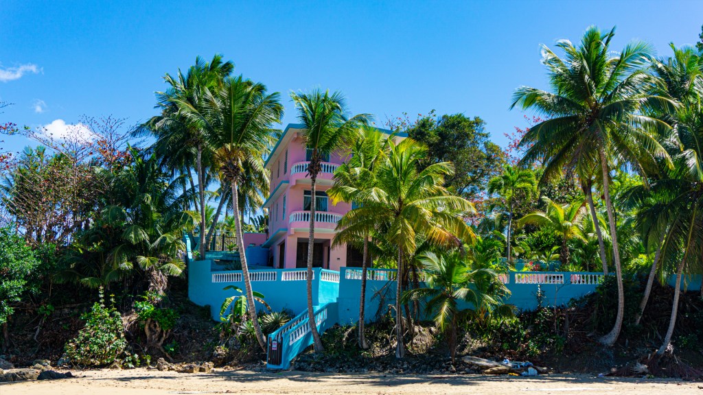 A colorful pink and blue house surrounded by palm trees on a beach in Rincon, Puerto Rico.