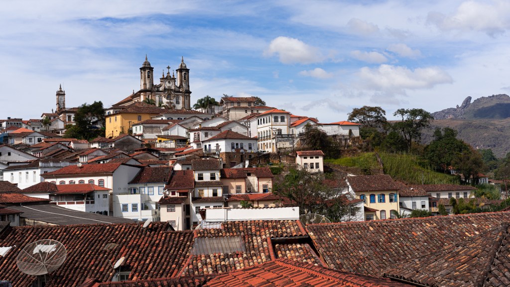 A photo of a city with white houses with orange tile roofs, leading uphill to a 18th century church.