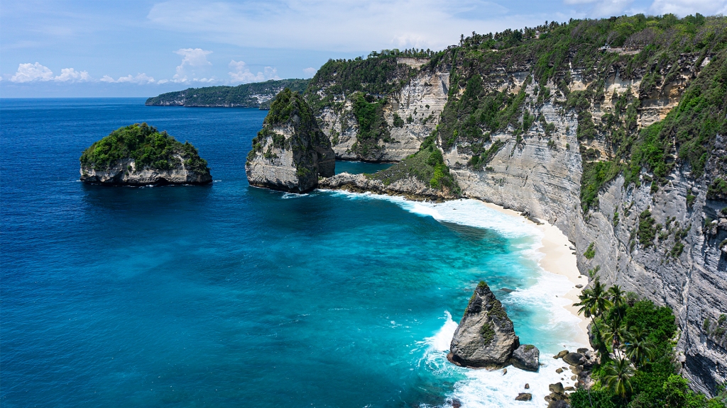 Diamond Beach in Nusa Penida, a small island off of Bali, Indonesia. A overlook of a vividly blue beach with pointy rock formations.