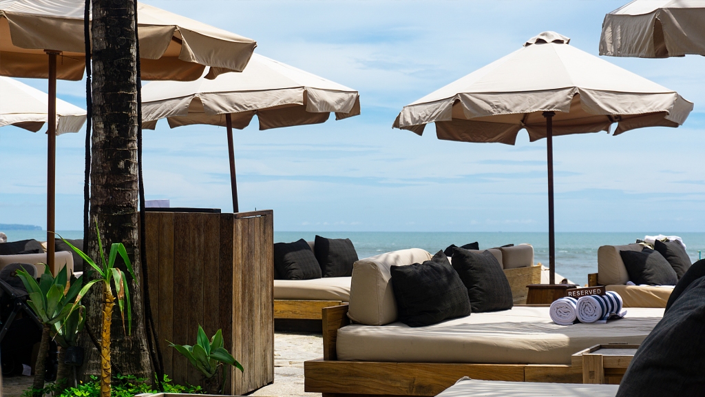 The Lawn, a beach club in Canggu, Bali on Canggu Beach. Umbrellas and daybeds for rent in front of a pool on the beach.