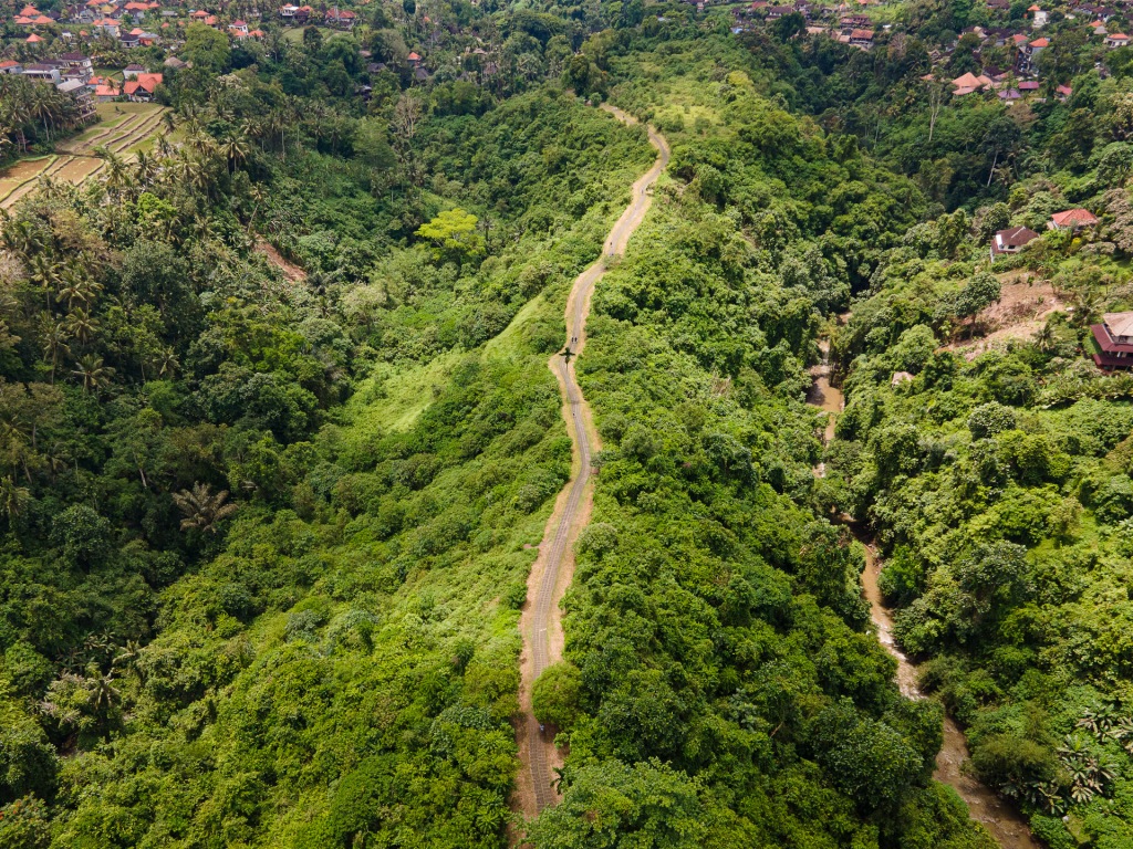 An aerial photograph of a long sidewalk at the top of a green mountain ridge, and a valley on either side.