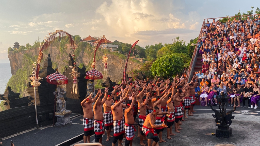 The Kecak Fire Dance Show at the Uluwatu Temple in Bali. The men are all standing together with their hands in the air during the sunset show.