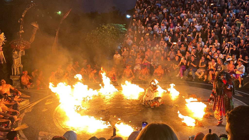 The Kecak Fire Dance at the Uluwatu Temple in Bali. A man dressed as a white monkey is sitting in the middle of a ring of fire, as another man in a costume is starting the fire.