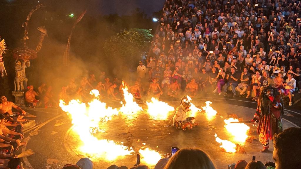 The Kecak Fire Dance at the Uluwatu Temple in Bali. A man dressed as a white monkey is sitting in the middle of a ring of fire, as another man in a costume is starting the fire.