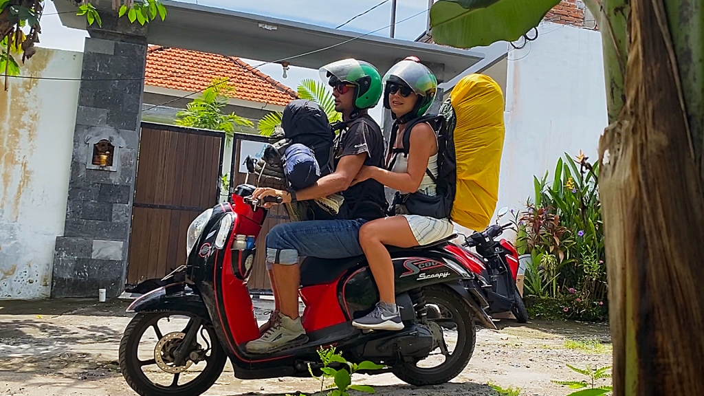 A man and a woman on a scooter while wearing backpacks.