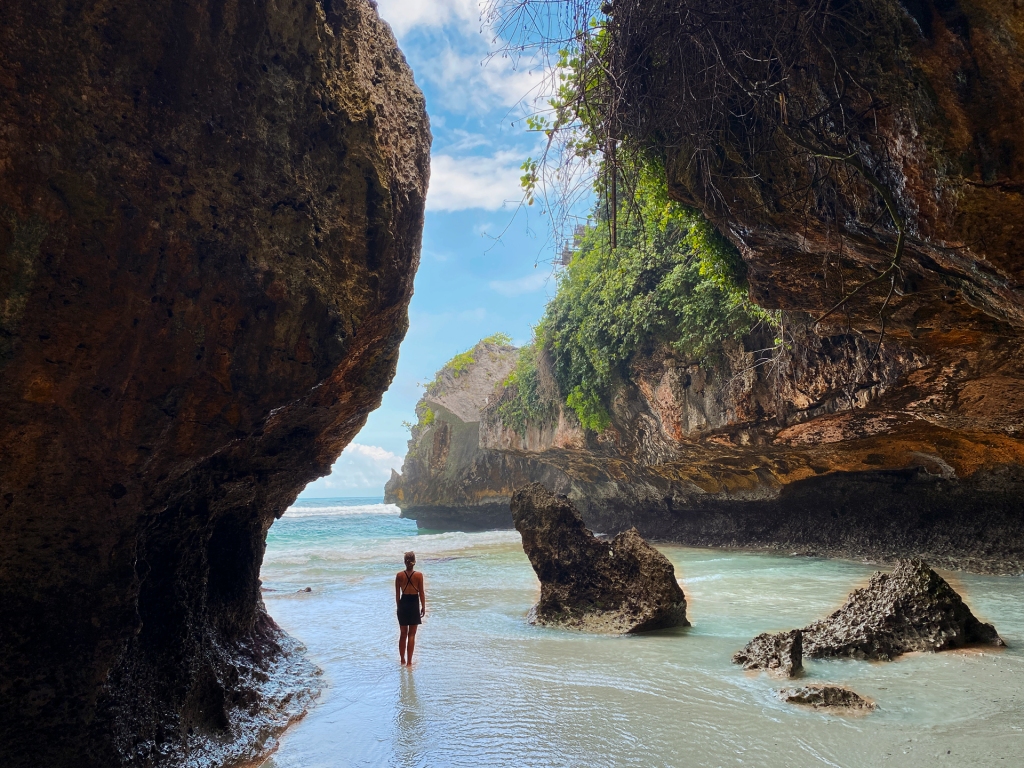 A woman standing on a beach with a cave-like rock formation.