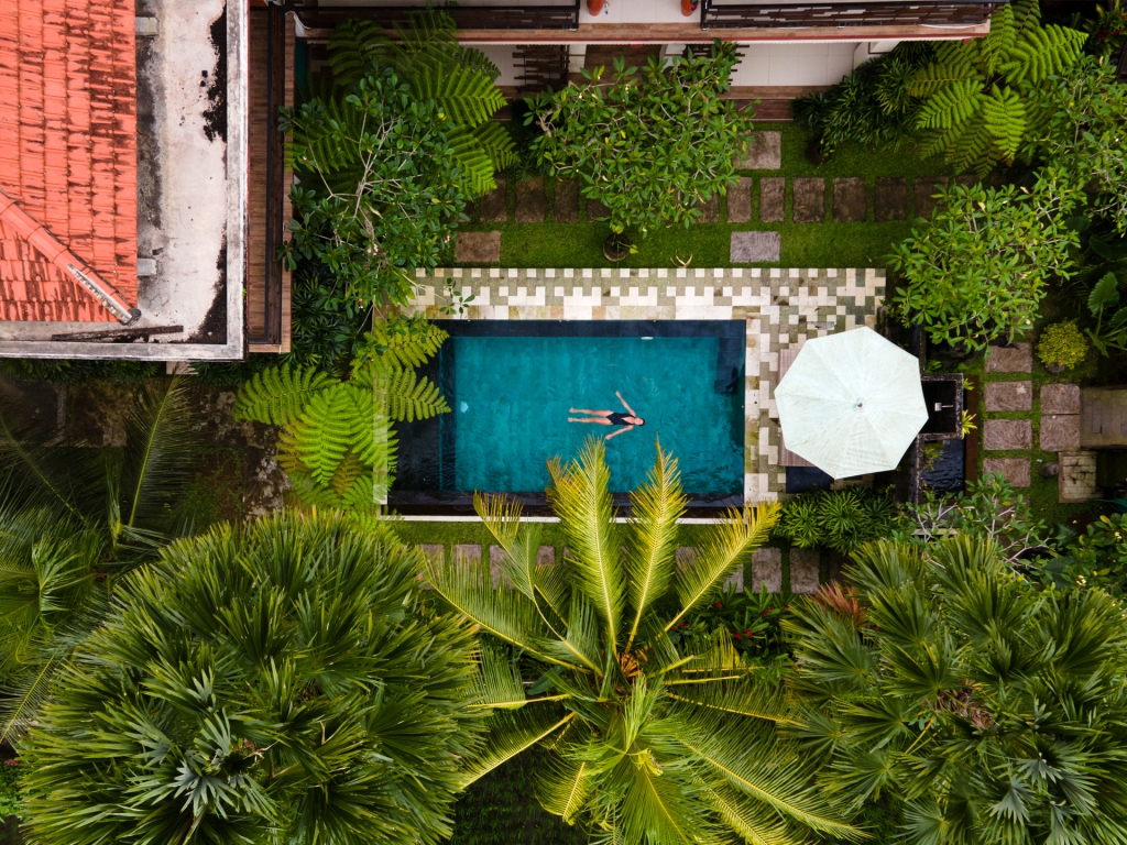 An aerial photograph of a woman floating in a rectangular pool at a villa in Ubud, Bali.