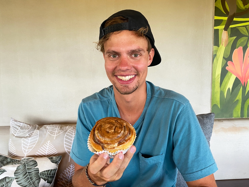 A man sitting in a restaurant holding a large cinnamon roll.