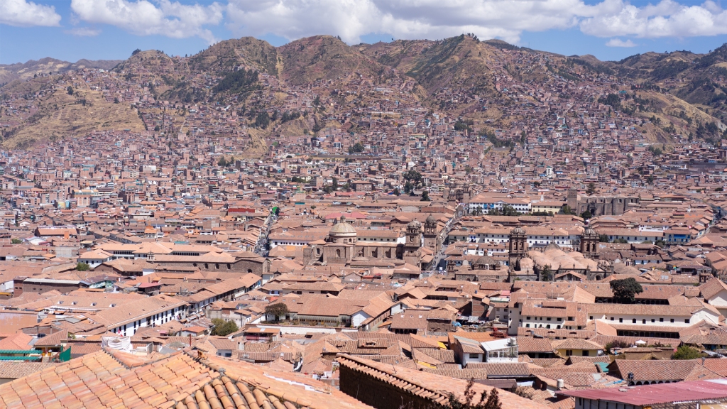 The city of Cusco, Peru in the historical district. Brown rooftops in front of a large mountain within the Andes mountain range.