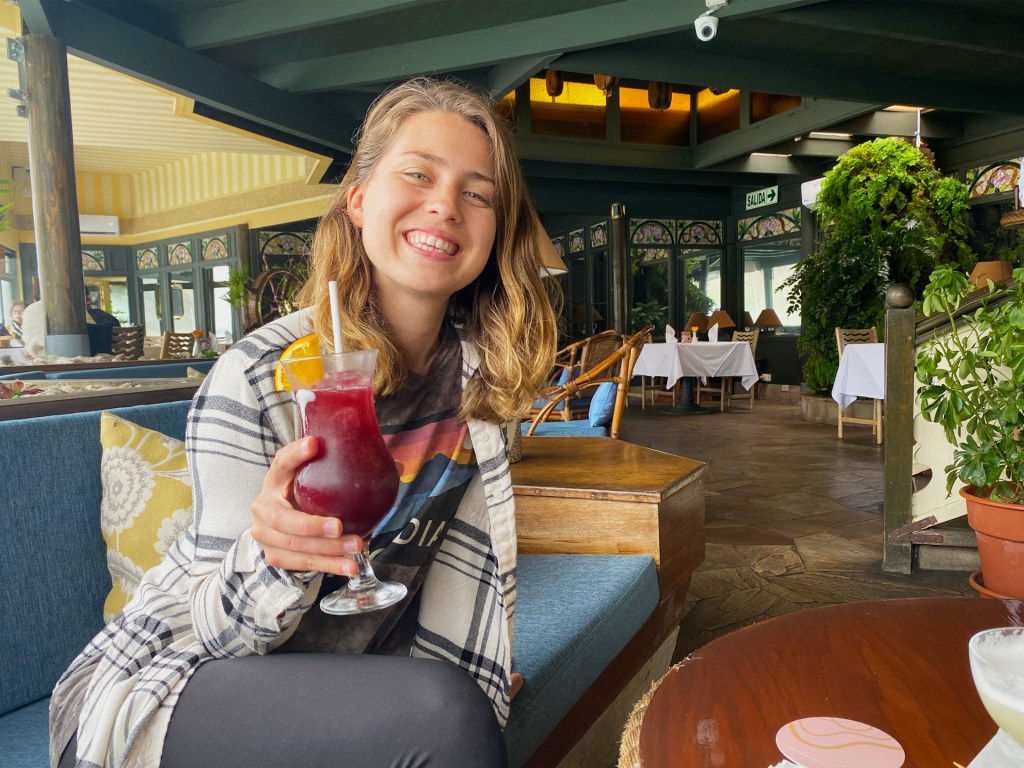 A woman in a restaurant holding a red cocktail with an orange slice on the rim.