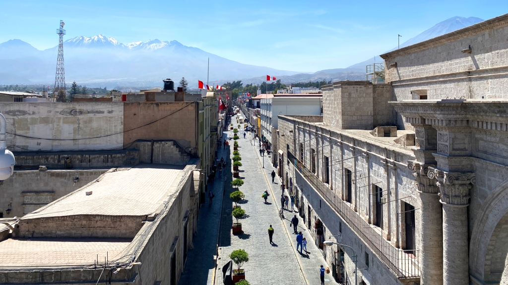 A historical street in Arequipa, Peru, with a snow-capped volcano in the distance.
