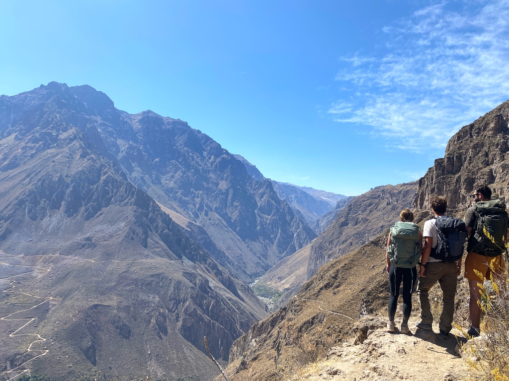 Three people wearing backpacks, standing at the top of Colca Canyon in Peru.