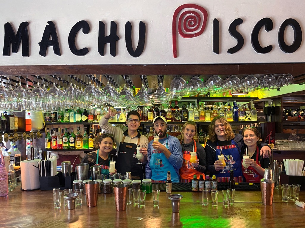 Five adults and one bartender standing behind a bar making pisco sours in Peru.