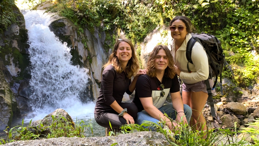 Three young adults posing in front of a small waterfall in Aguas Calientes, Peru.