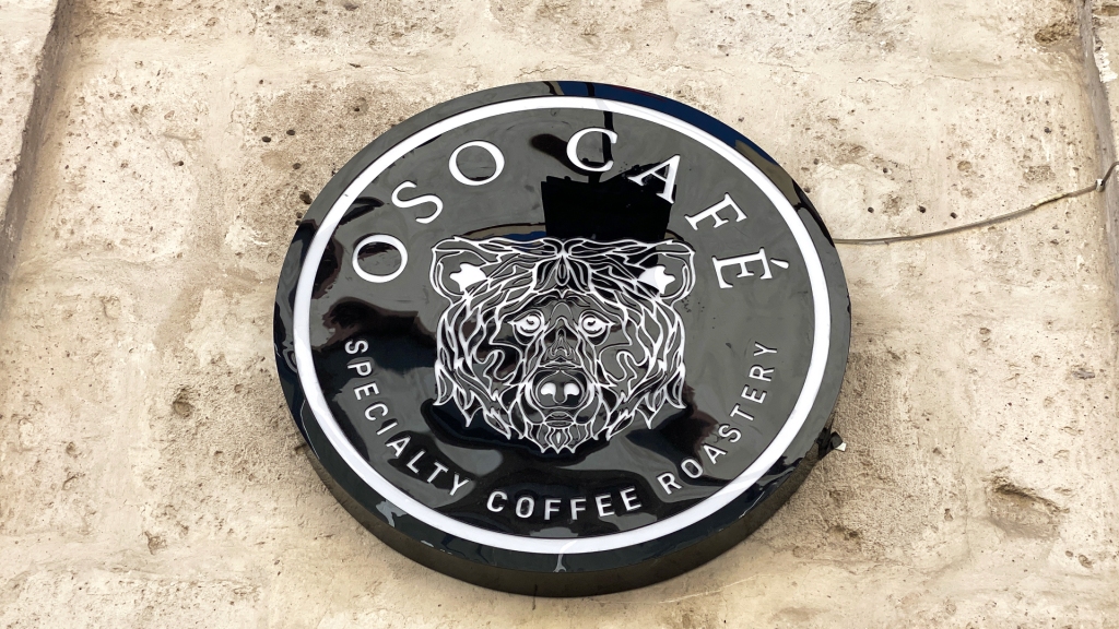A circular sign on a white, stone wall reading: Oso Café Specialty Coffee Roastery.