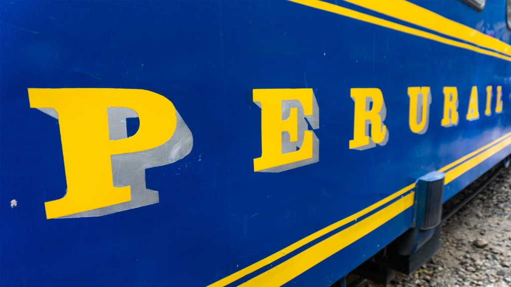 A close up picture of the words on the side of a blue and yellow train reading: Peru Rail.