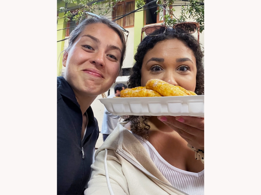 Two women holding up a plate of picarones, a type of sweet potato doughnut.