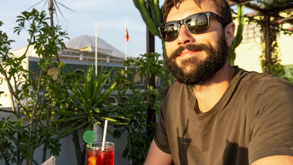A man drinking a cocktail on a rooftop patio, with Volcano Misti in the background.