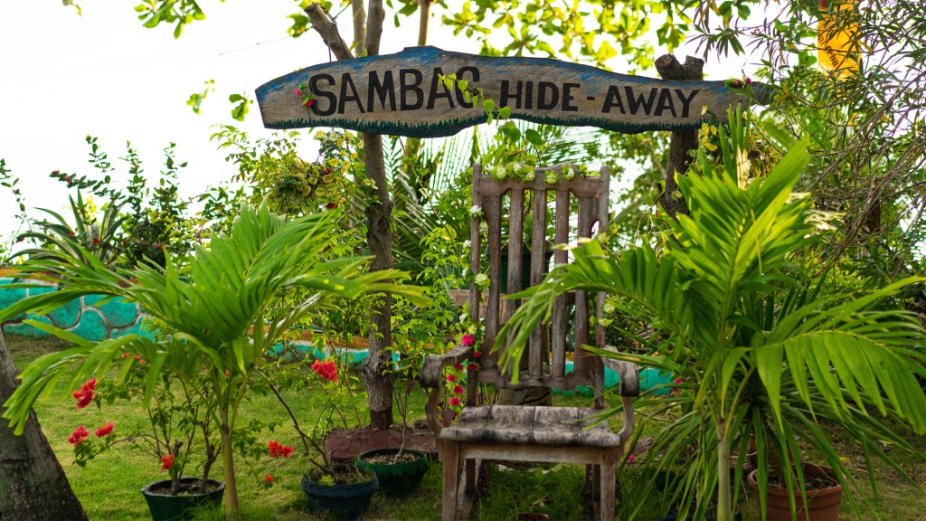 A wooden chair in a green garden filled with palm leaves and a sign reading, Sambag Hide-Away in the Philippines.