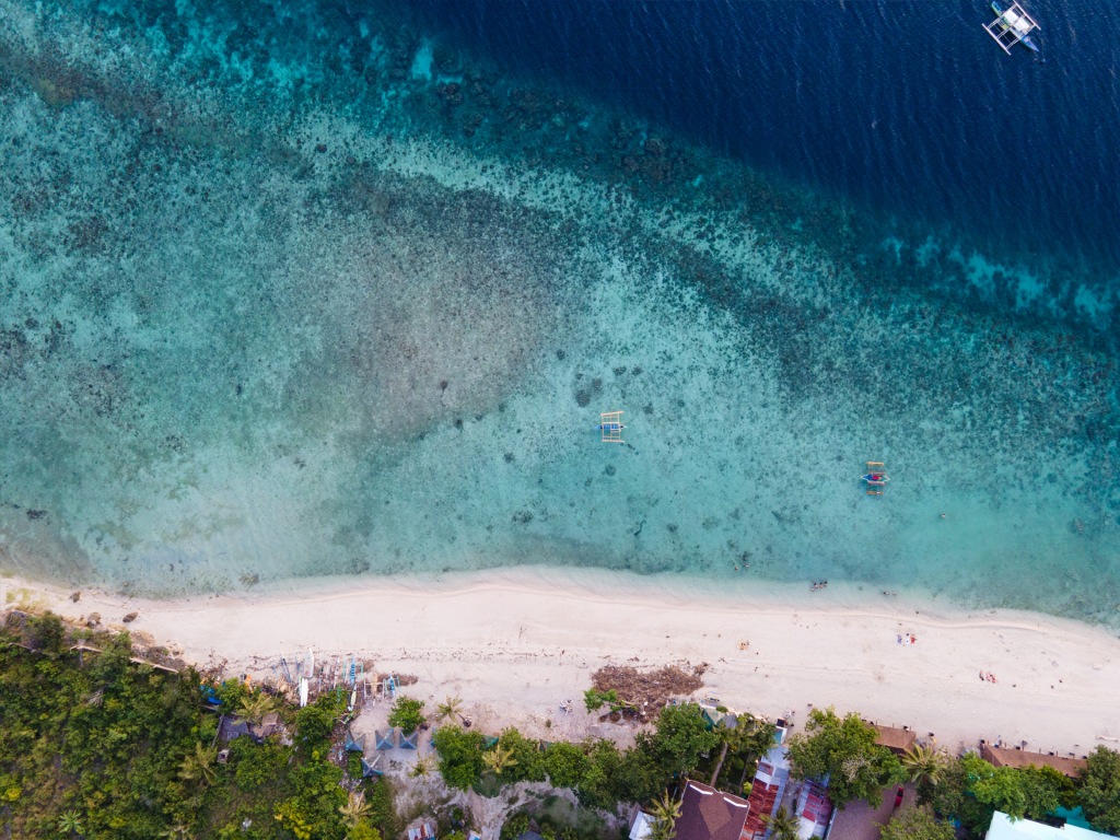 An aerial photograph of White Beach in Moalboal, Philippines. A beach with white sand and blue water.