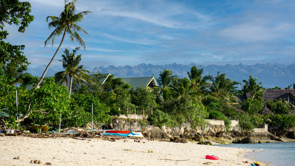 White Beach in Moalboal, Philippines. A beach lined with palm trees and mountain peaks in the distance.