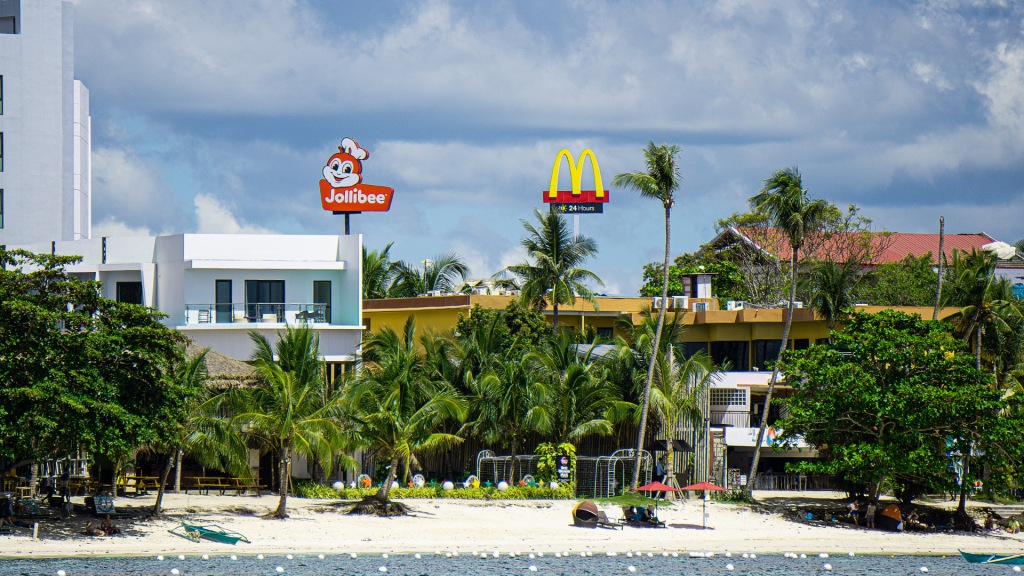 A photograph of Alona Beach in Panglao, Philippines, Behind the beach is a sign for McDonald's and Jollibee fast food restaurants.