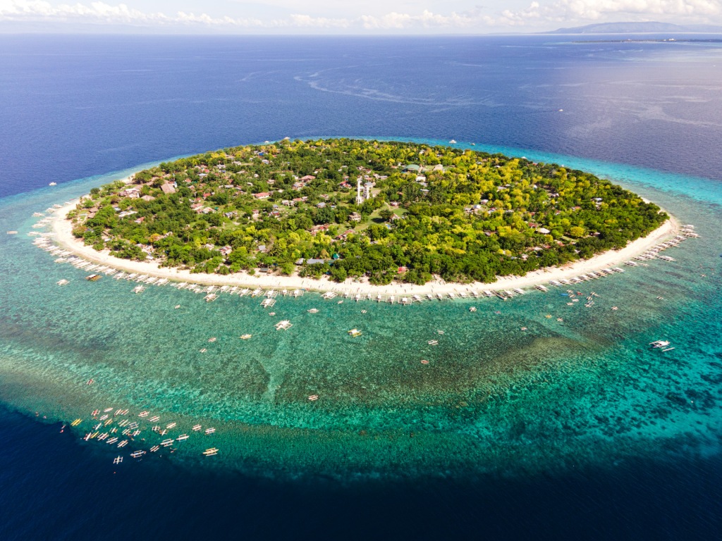 A drone photo of Balicasag island in the Philippines. A small, round island surrounded by very blue water.