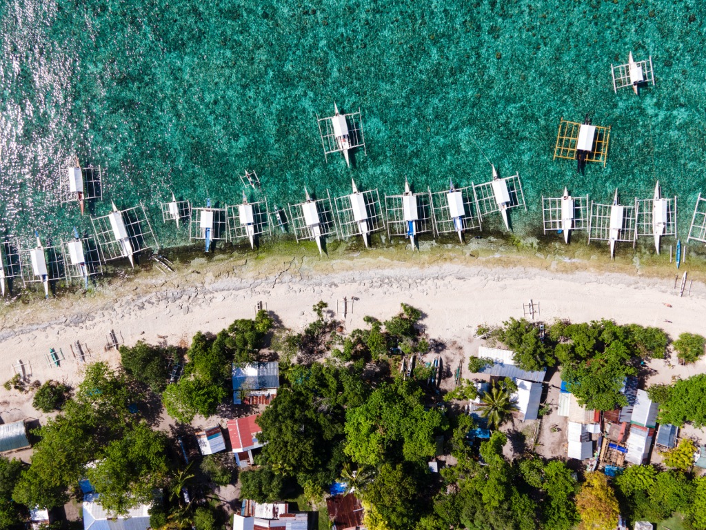 A drone photograph looking down at the beach lined with white boats on Balicasag Island in the Philippines.