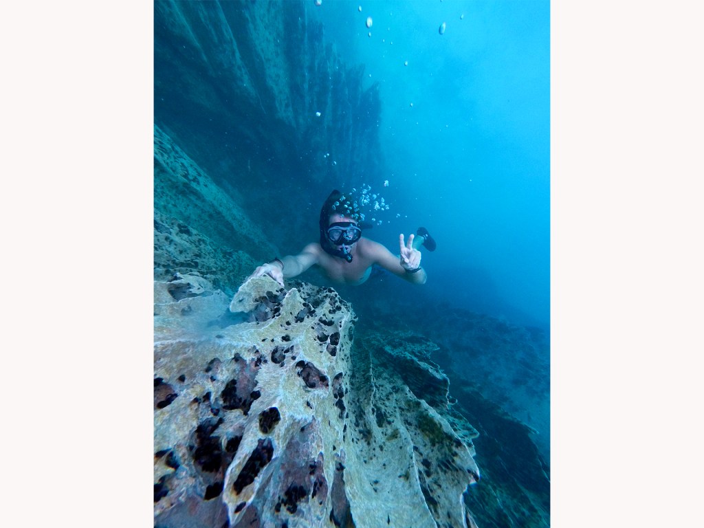 A man diving in Barracuda Lake in Coron, Philippines. The water is a clear blue and there a staggering limestone cliffs under the water.