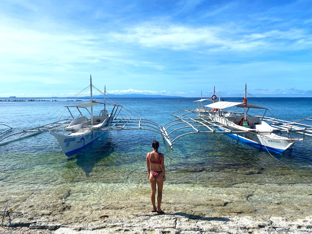 A woman standing in front of two wooden boats in Balicasag Island, Philippines.