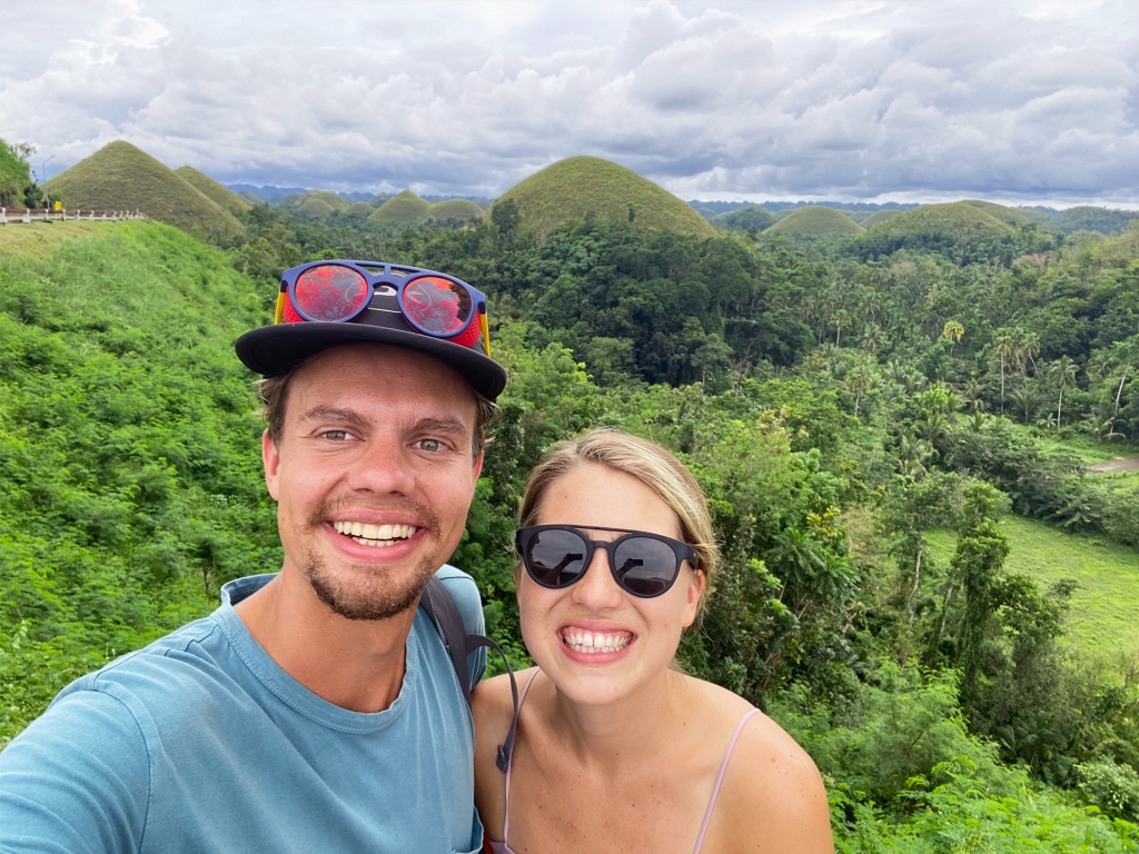 A man and a woman taking a selfie in front of the Chocolate Hills in Bohol, Philippines.