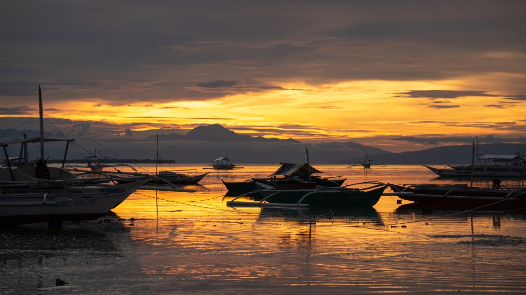 A bright orange sunset over the ocean, with dark mountains in the distance. Panglao, Philippines.
