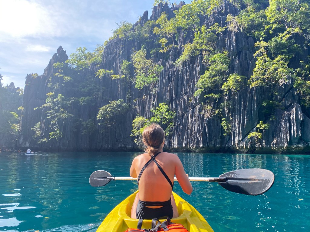A woman kayaking towards large limestone cliffs in Coron, Palawan, Philippines.