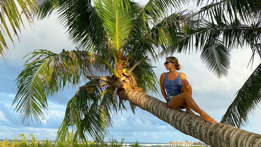 A woman sitting on the trunk of a palm tree in front of the ocean in Siargao, Philippines.