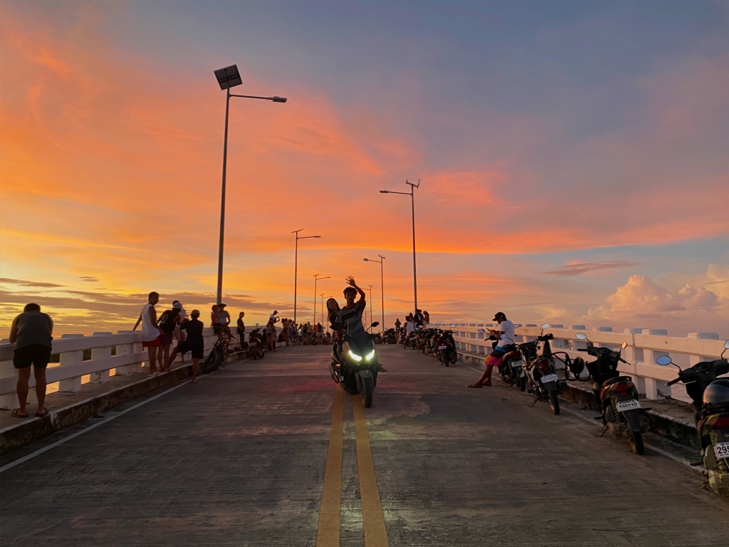 A person riding a motorbike down the middle of a bridge at sunset, in Siargao.